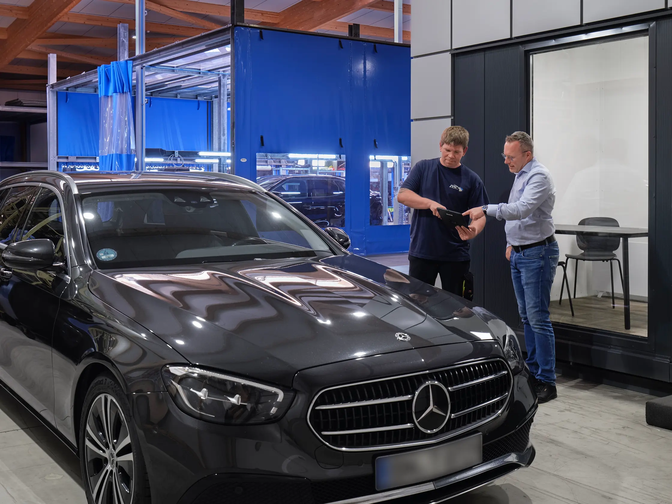 Geschäftsführer Michael Jost spricht mit einem Mitarbeiter am Tablet, während ein schwarzer Mercedes-Benz im Vordergrund steht.