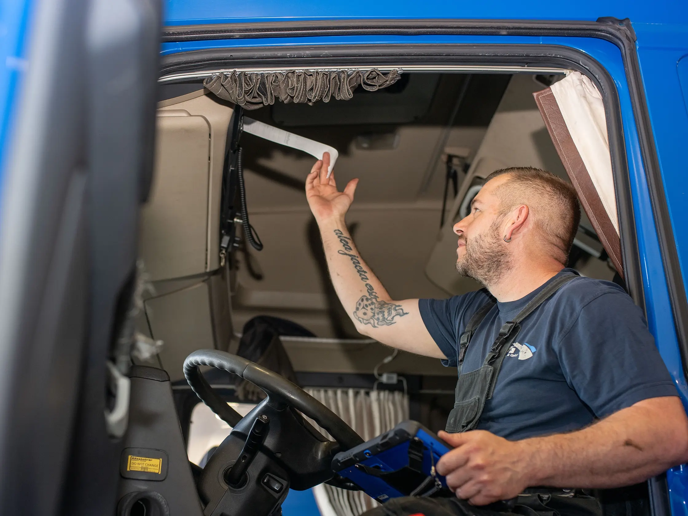 Ein Mitarbeiter von JVG sitzt im Fahrerhaus eines blauen Fahrzeugs und hält ein Stück Papier in der Hand. Der Fahrer trägt ein schwarzes T-Shirt.